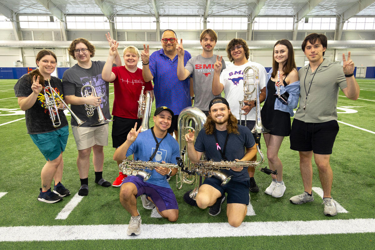 Mustang Band members pose on an indoor football field with their instruments during practice