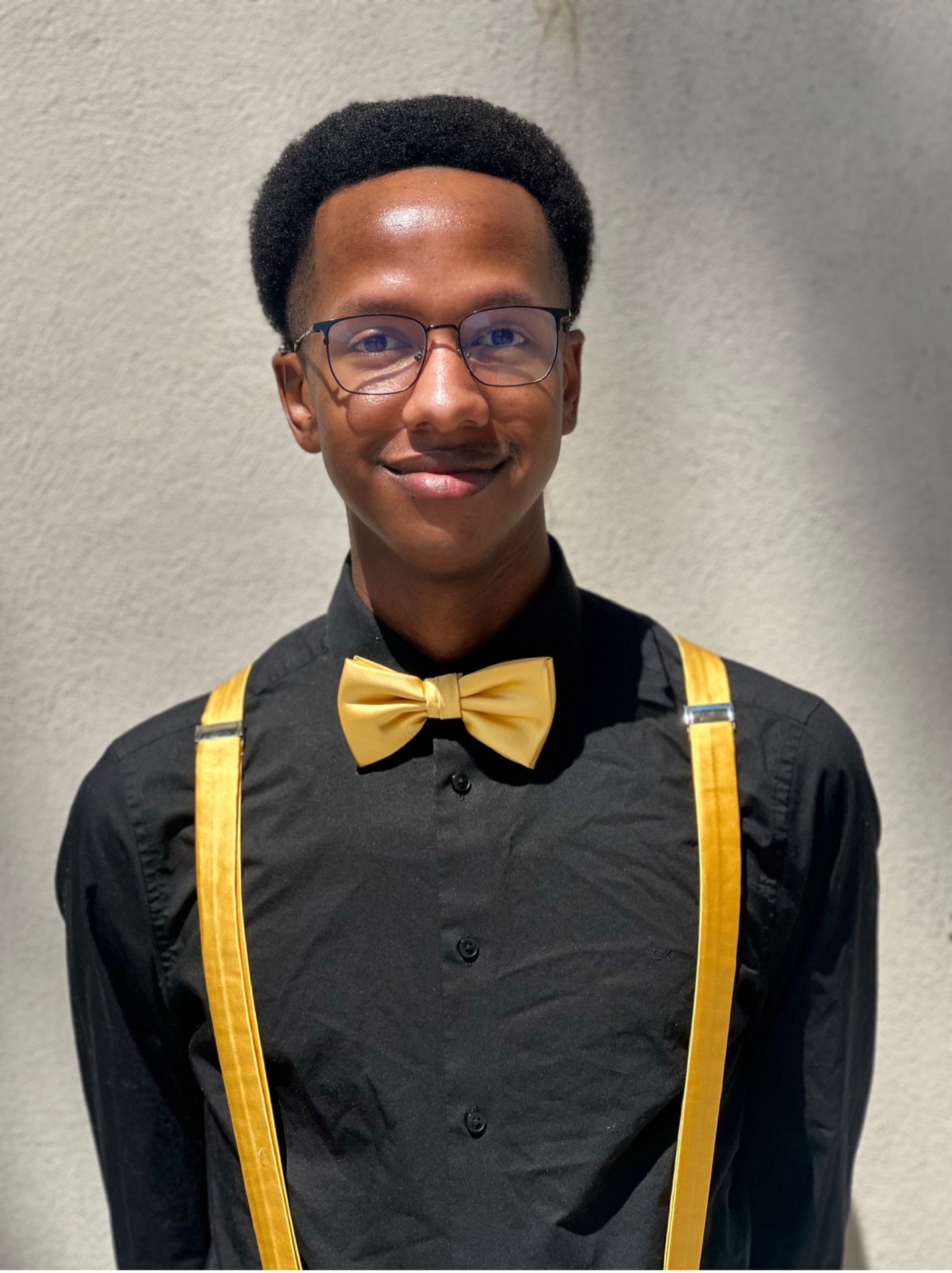 Music composition student Paul Johnson poses in a black shirt with yellow suspenders and glasses