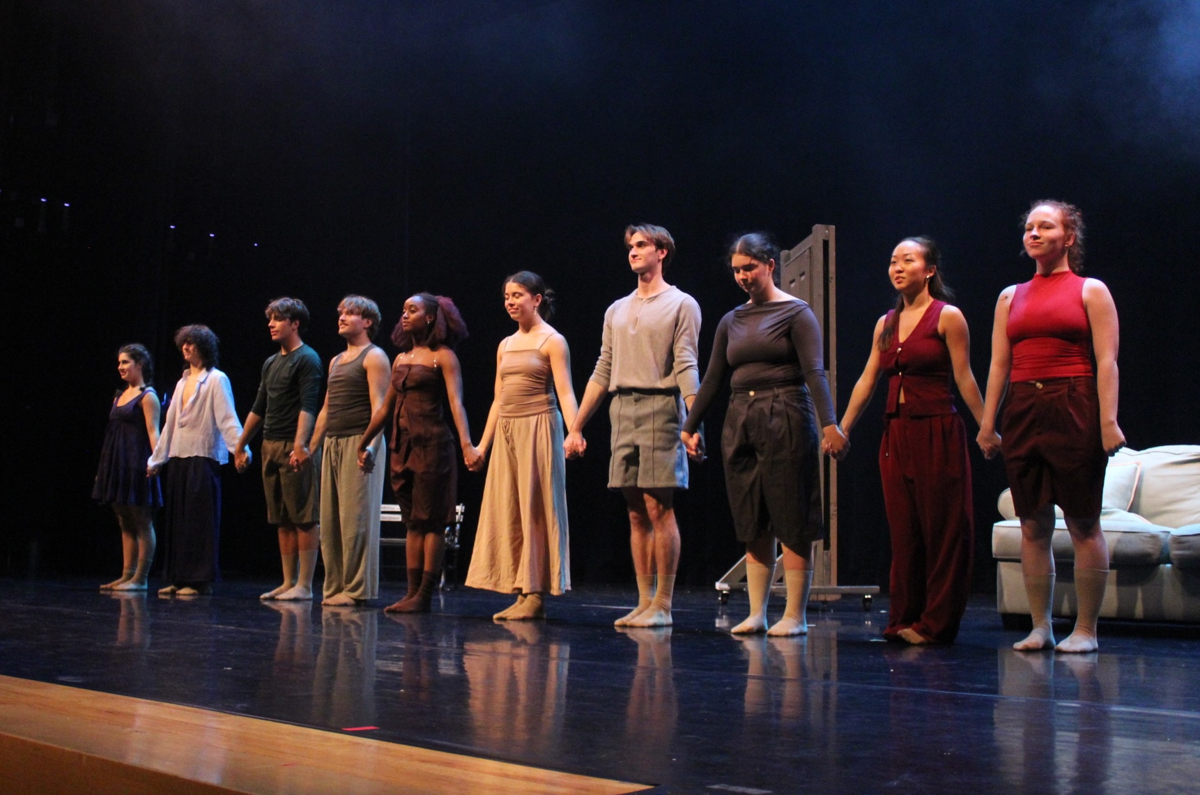 Ten dancers stand on stage holding hands after finishing a show
