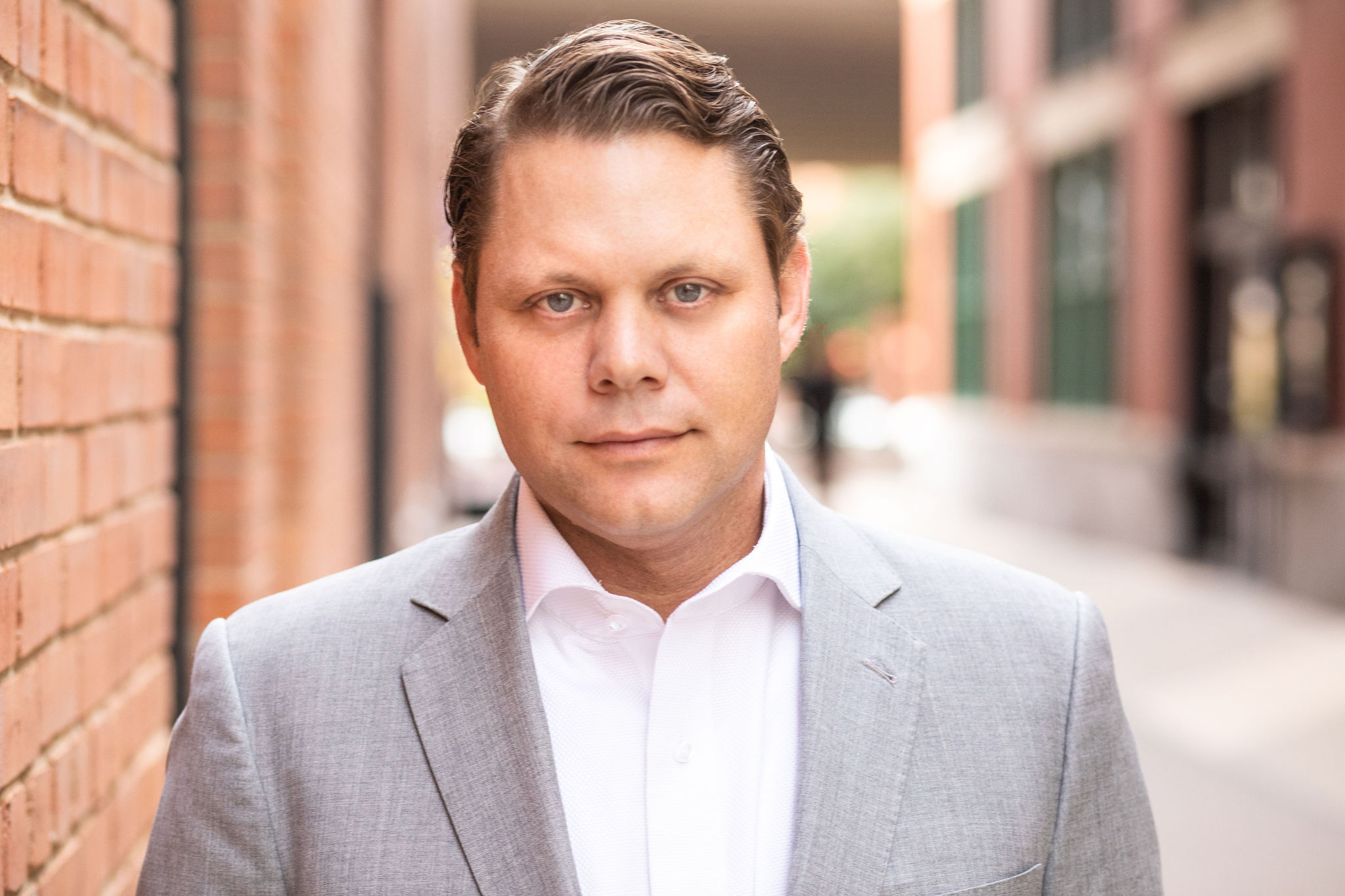 Investor and entrepreneur Trey Bowles poses in front of a brick wall in a gray suit