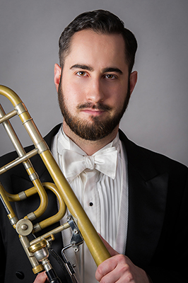 Music alum Derek W. Hawkes poses with a trombone wearing a suit