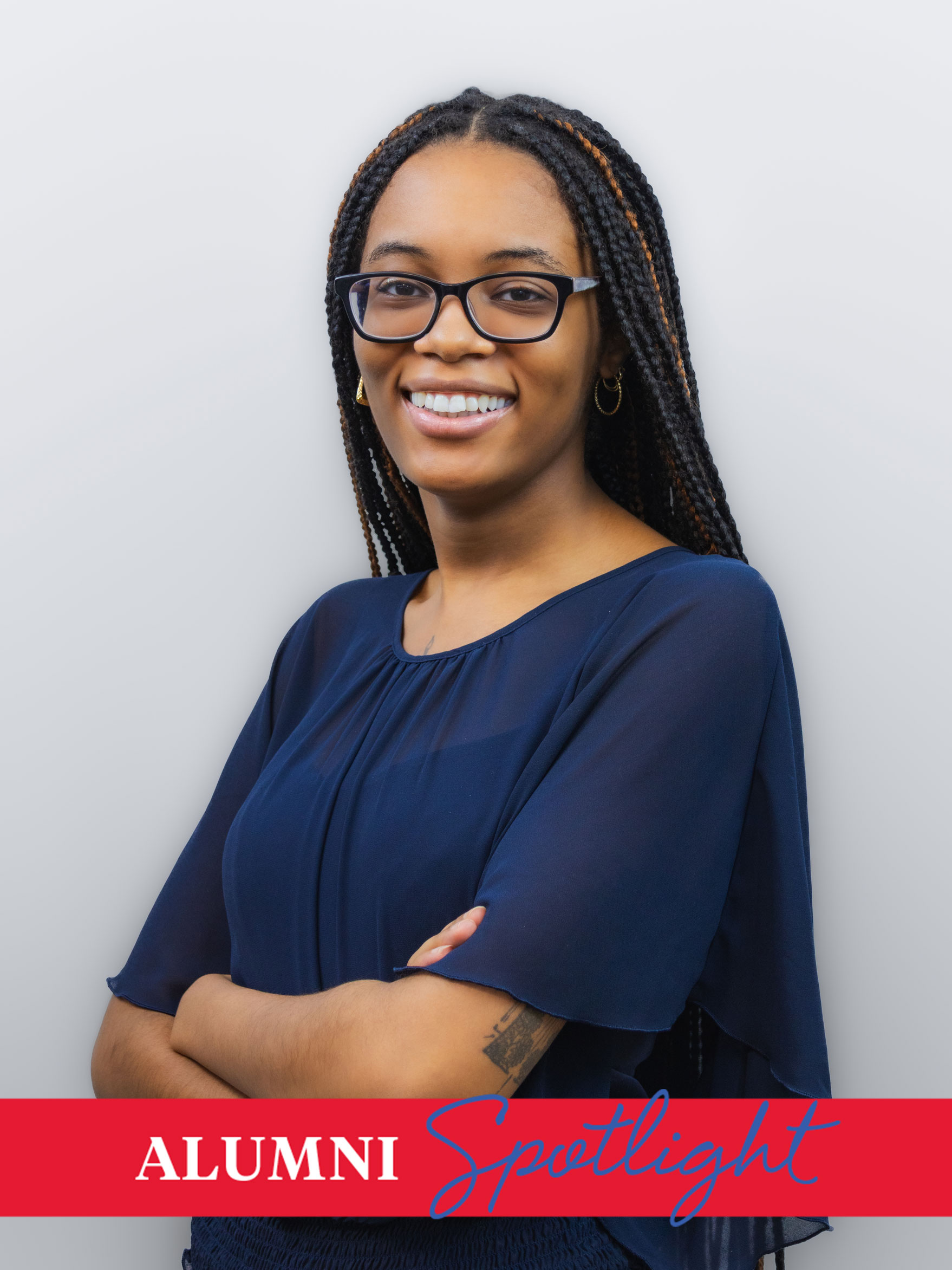 Creative Computation alum Makayla Alston poses in a navy blouse and black frame glasses against a gray background