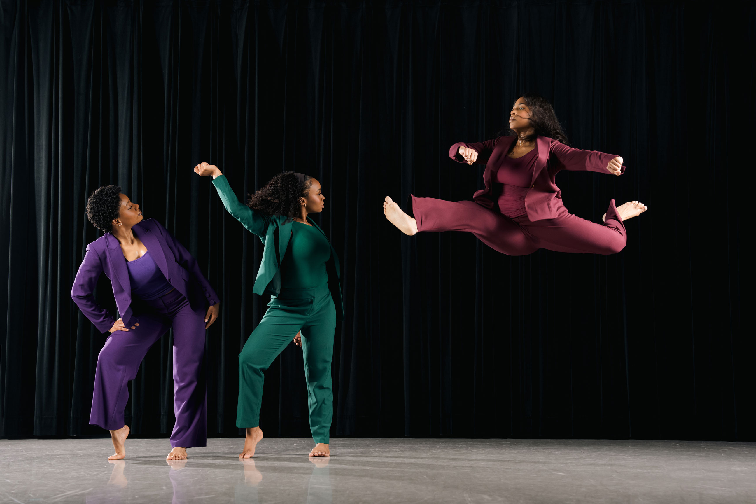 Three dancers on stage with one leaping through the air