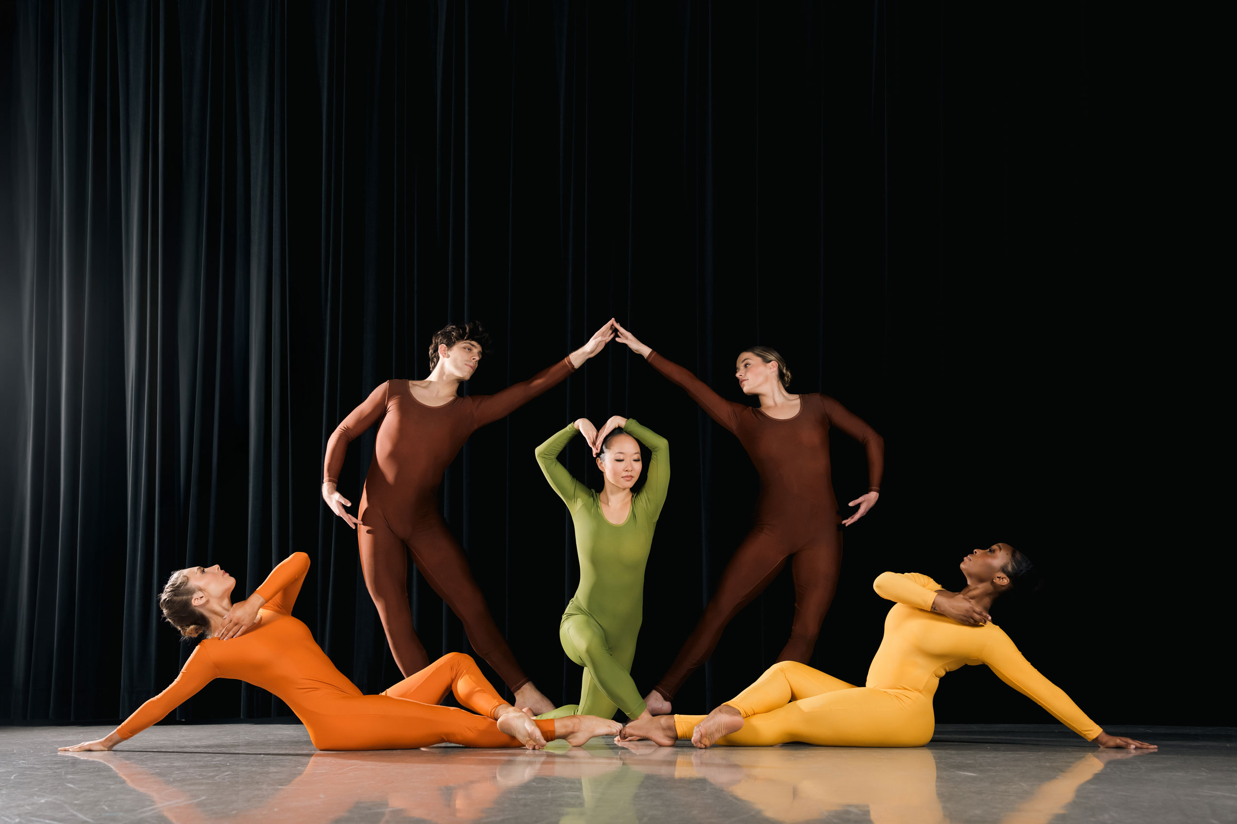 Five dancers posed on stage in colorful leotards