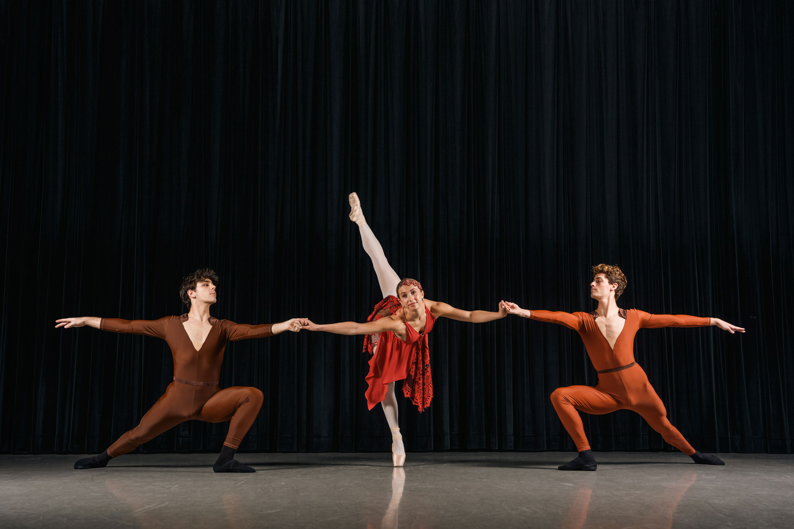 One female ballet dancer poses between two male ballet dancers on stage in costume