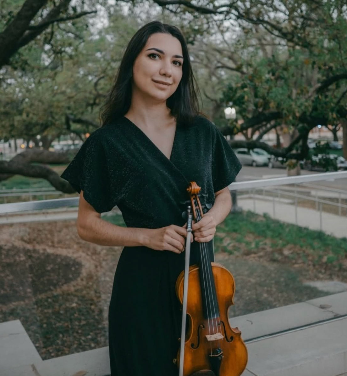 Violin student Daria Oleinik poses with her violin in a black dress outside