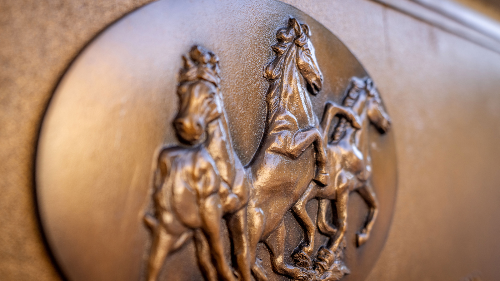 A bronze relief depicting three horses in motion on a circular plaque.