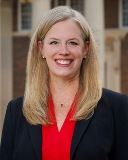 a woman in a red shirt and black suit in front of a building with columns