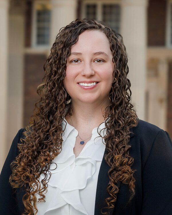 a woman in a white shirt and black suit in front of a building with columns