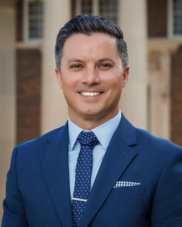 a man in a ight blue shirt and blue suit in front of a building with columns