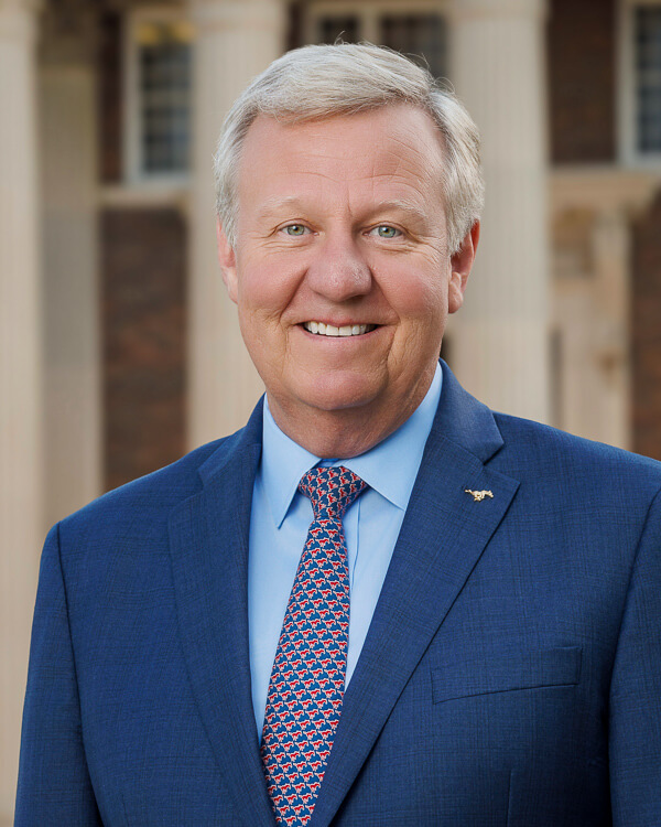 a man in a light blue shirt and blue suit in front of a building with columns