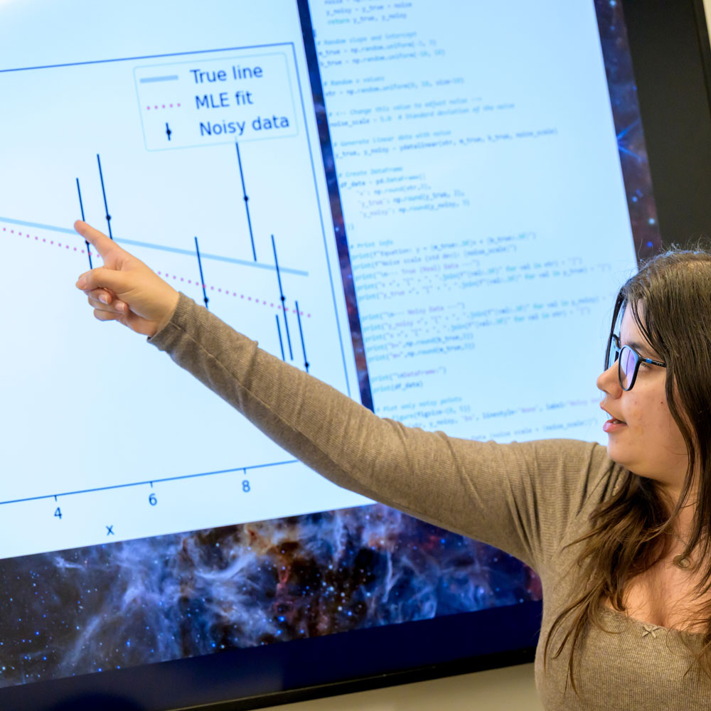 Student analyzes data visualizations and computer code on a large digital display during a technology-focused research project.