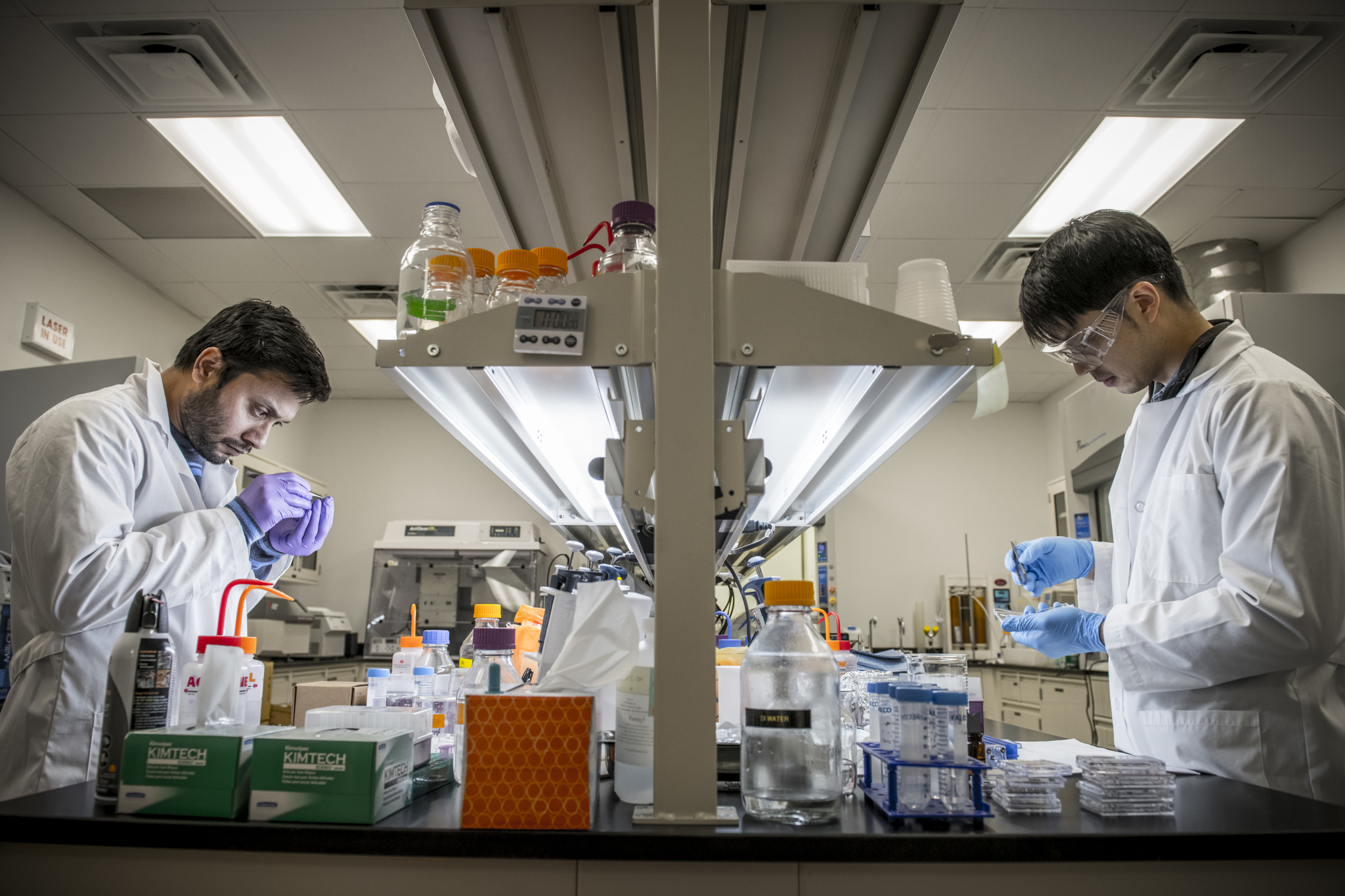 Two people in lab coats looking down on a table with research instruments