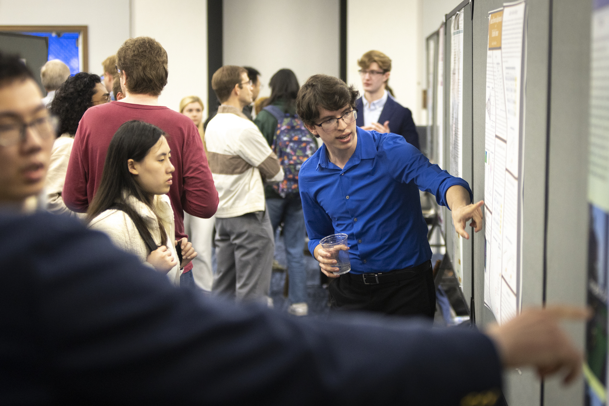 photo of an academic poster session with a student pointing to his poster