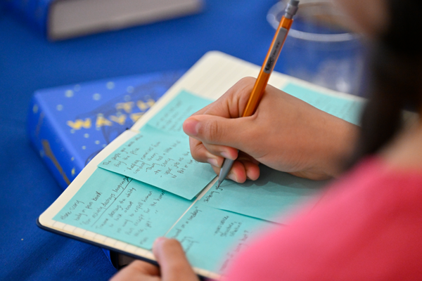 Hilltop Scholars Student writing on blue sticky notes in a journal during an event