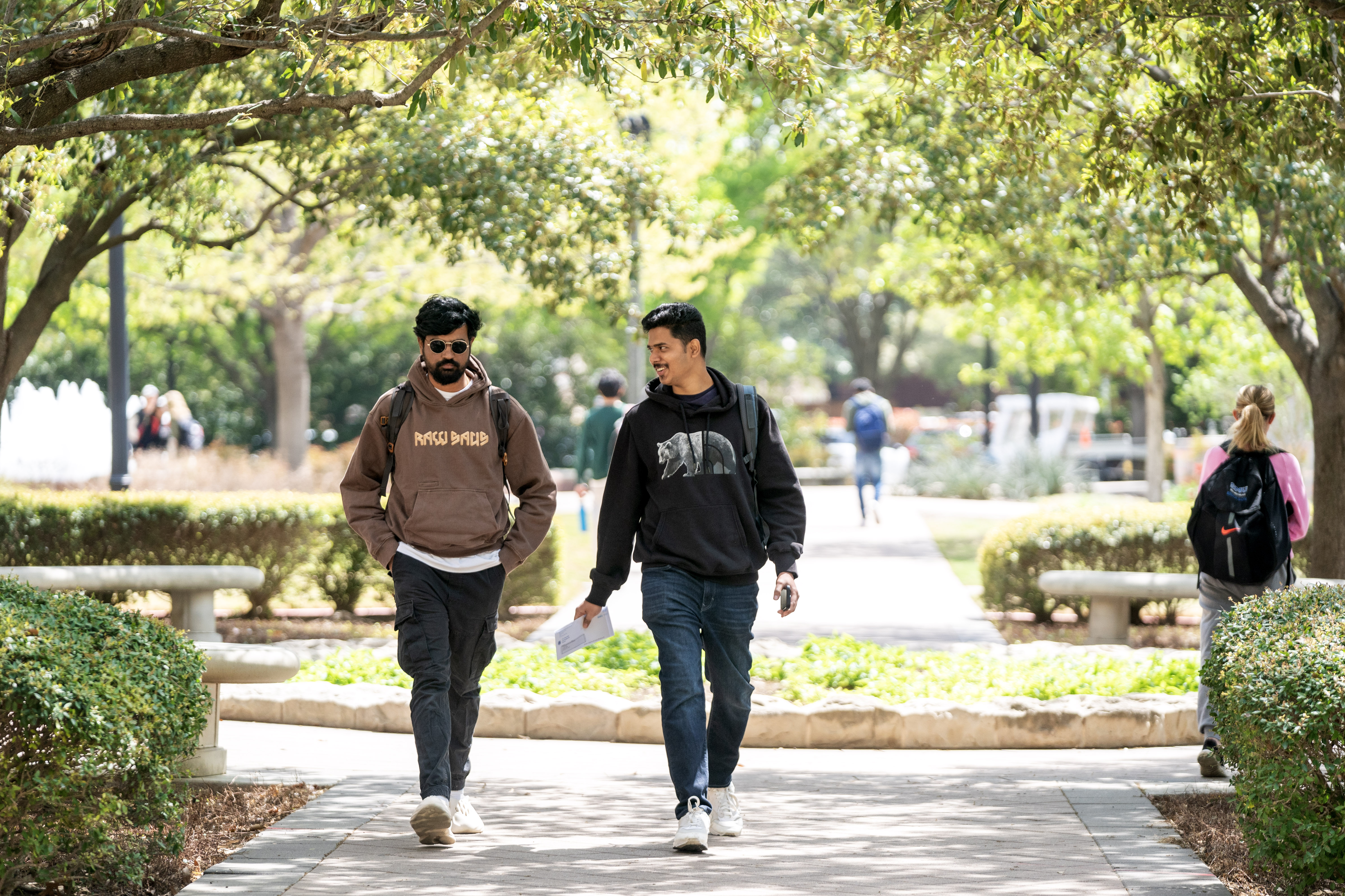 Two students walk down a path with trees framing the shot