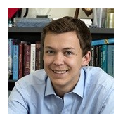 Ian Johnson is a white man with short brown hair. He is wearing a light blue button up and poses in front of a bookshelf with books.
