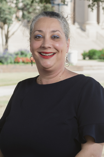 Dr. Joan Arbery wears a black top and stands outside with Dallas Hall steps in the background