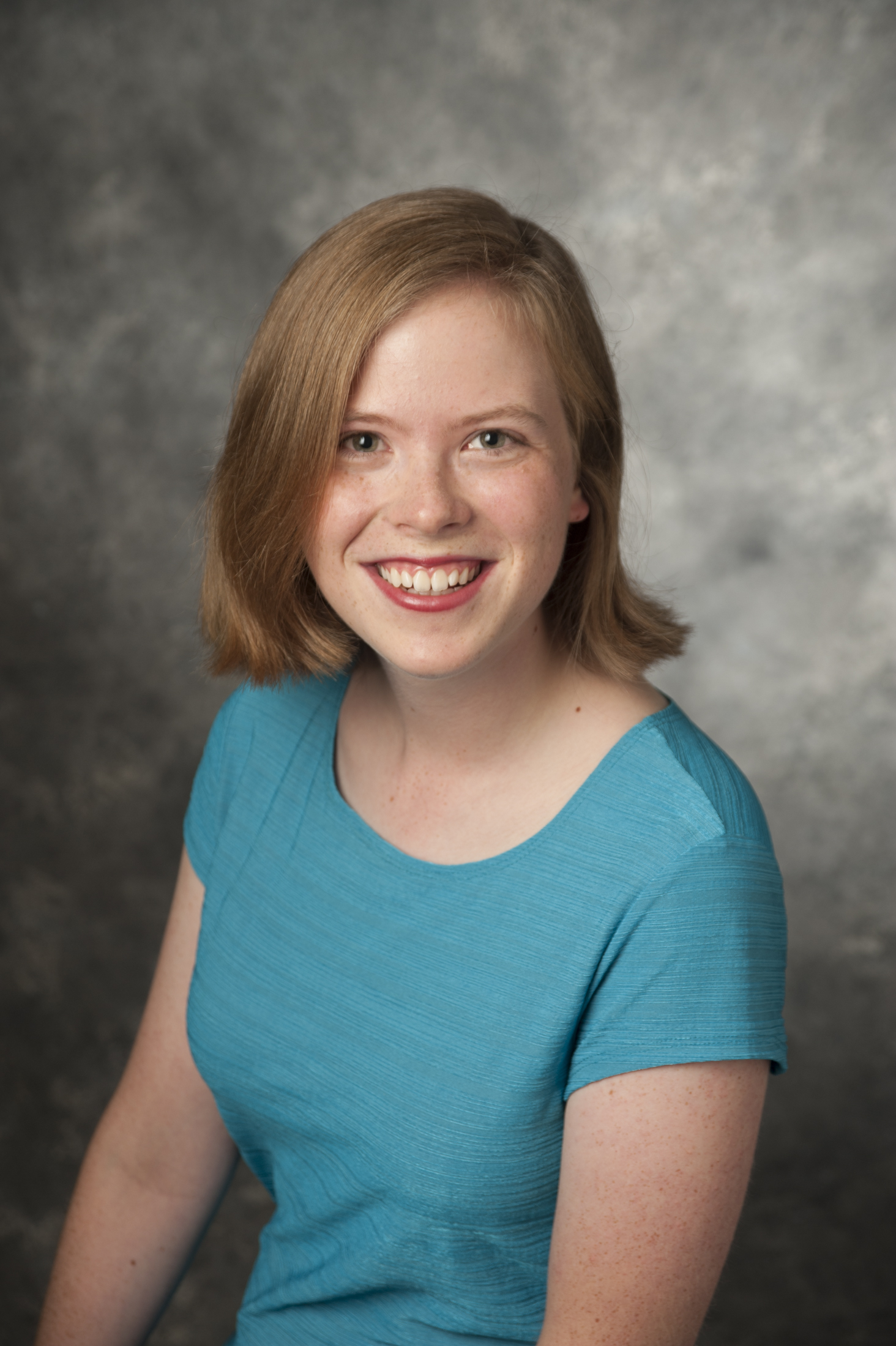 Hope Anderson is a white woman with red hair to her chin. She wears a turquoise dress.