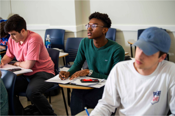 3 students taking notes at their desks in a classroom