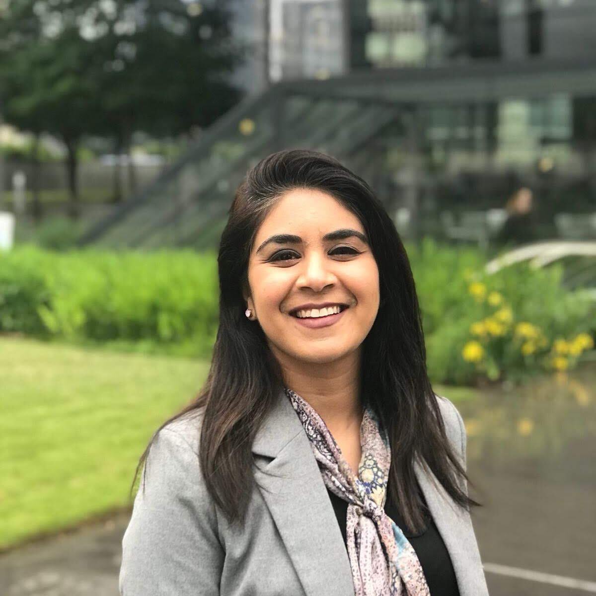 Photo of Amra Sayed smiling and standing on a lawn in front of a building