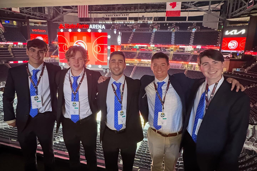 Five SMU Sport Management students pose in business attire with conference credentials inside State Farm Arena during the National Collegiate Sport Sales Competition finals in Atlanta.
