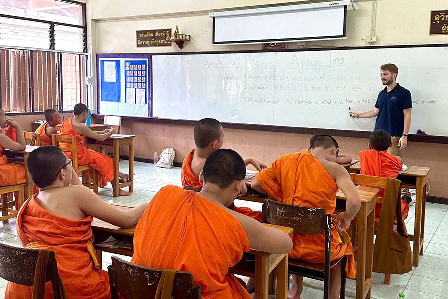 Student teacher earning an Educational Studies minor at the Simmons School of Education leading an English lesson for Buddhist novice students in ochre robes in a Chiang Mai, Thailand classroom
