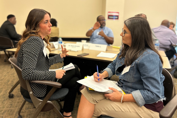 Two women talking, one taking notes