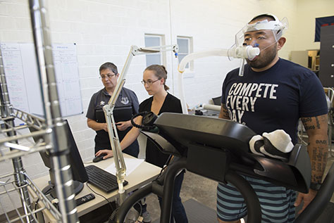 Simmons student on treadmill with breathing apparatus while professors monitor.