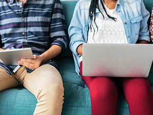 Two persons sitting on a couch working together on their devices.