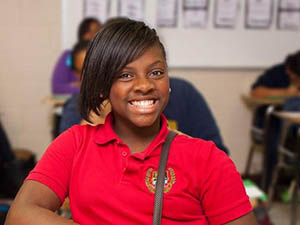 A smiling girl in a classroom with other students.