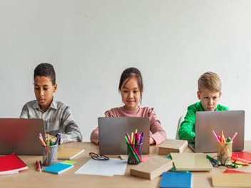 Middle school students are working on laptops together, sharing desk.