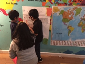 A group of children in a school classroom studying a map on the wall, showing curiosity and teamwork.