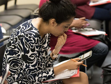 A woman seated in a chair, looking at her cell phone and handouts.