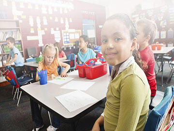 A classroom scene featuring children at desks, participating in lessons and collaborating on schoolwork.