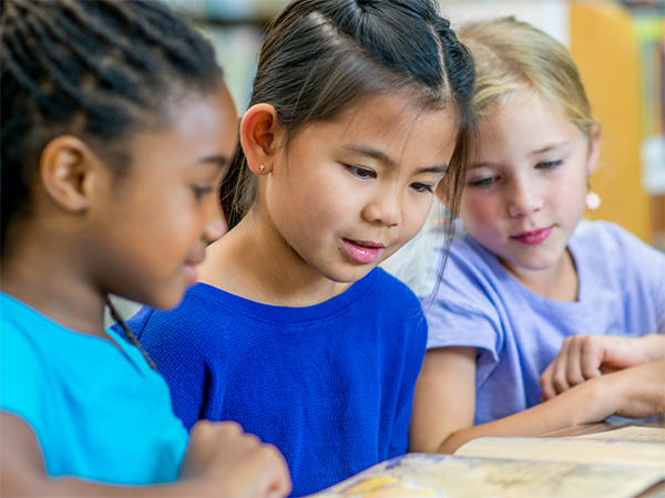 Three elementary aged school reading book together.