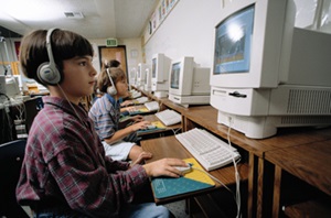A young boy with headphones on, participating in a reading intervention session in his first-grade classroom.