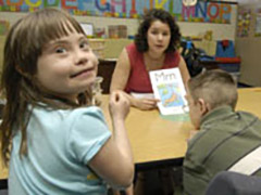  An instructor and two children sit at a table, engaged with books, highlighting a reading program for students with disabilities.
