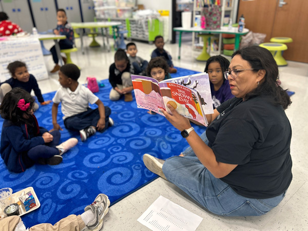 In a classroom, a teacher engages children, in an elementary classroom, by reading a story.