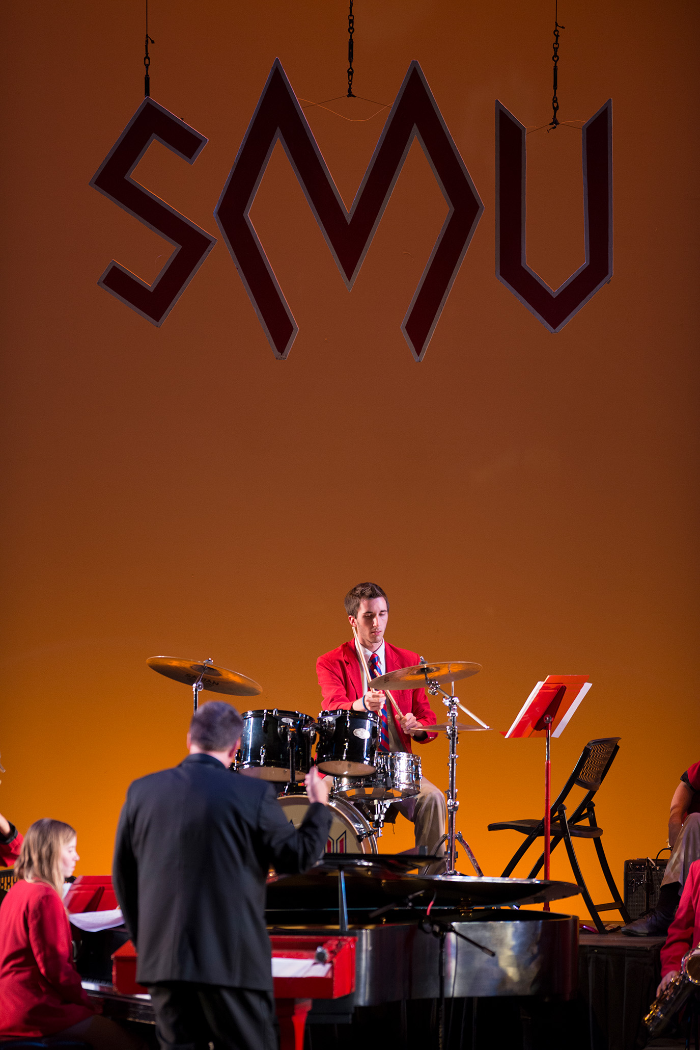 student playing drum set with SMU diamond M logo hangin above at pigskin revue