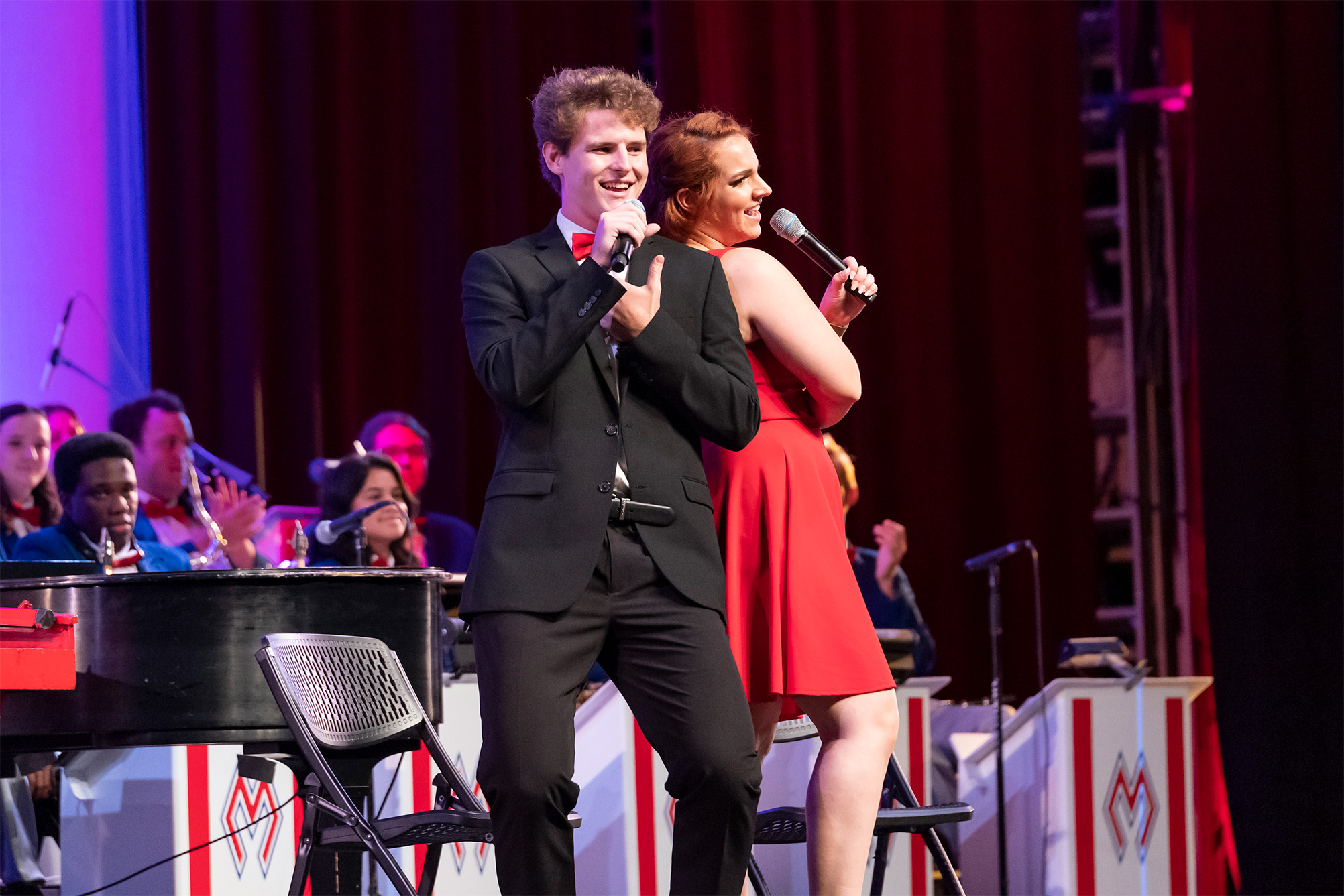 two students standing back to back in front of band signing at pigskin revue