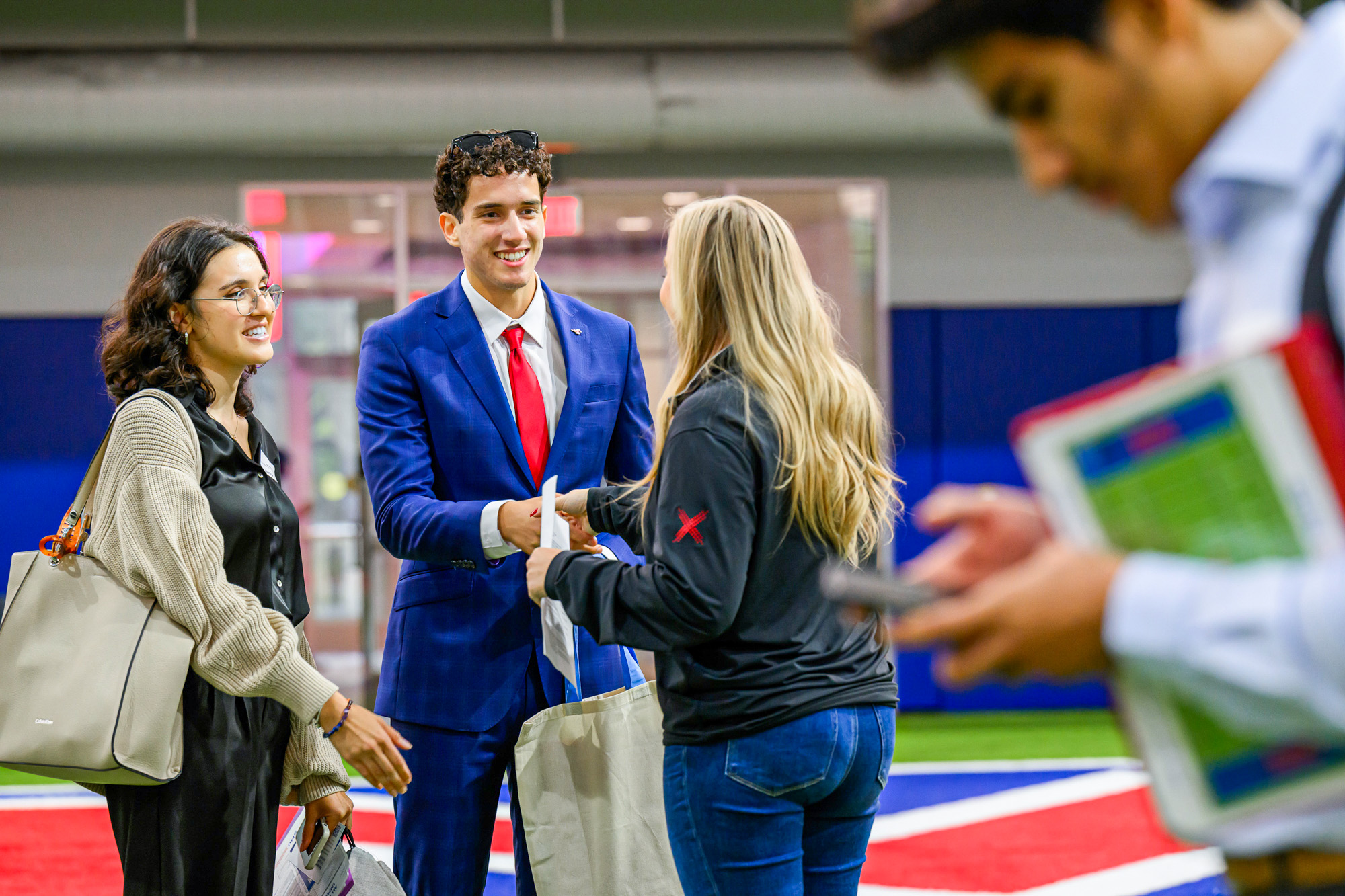 student and employer standing and shaking hands with another student standing beside them talking and smiling