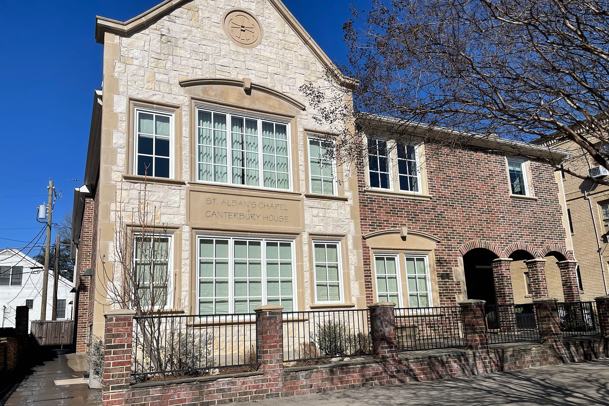 exterior photo of building, lights stone with red and brown brick, white trimmed windows, arched entryway to porch, trees and bushes around building