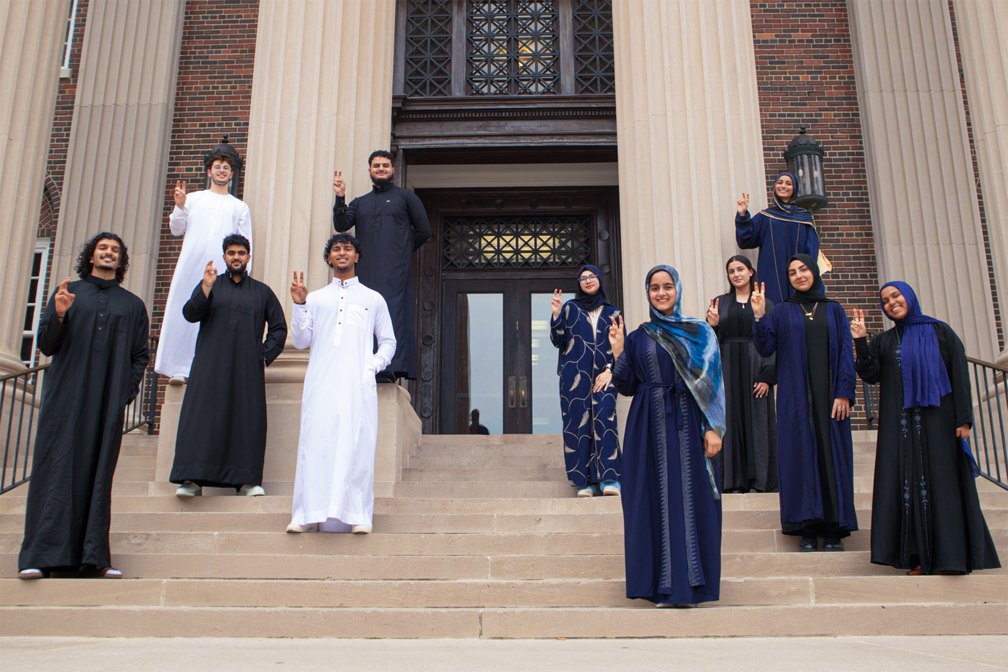 group of students standing on stairs in front of building in traditional islamic clothing