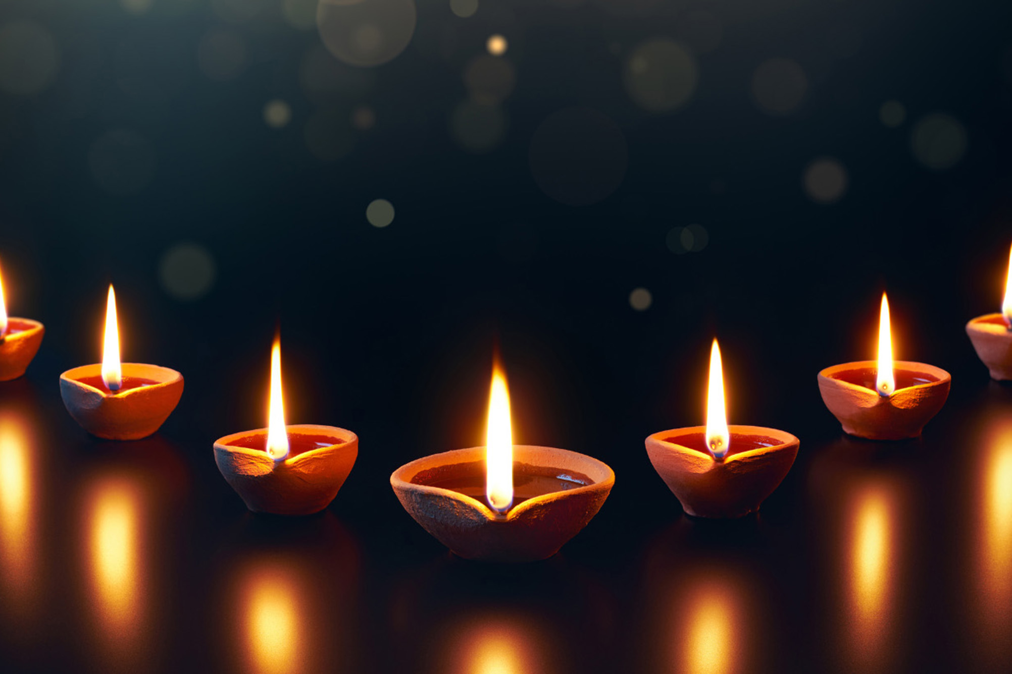 row of small candles in a "v" shape with flame on a black background