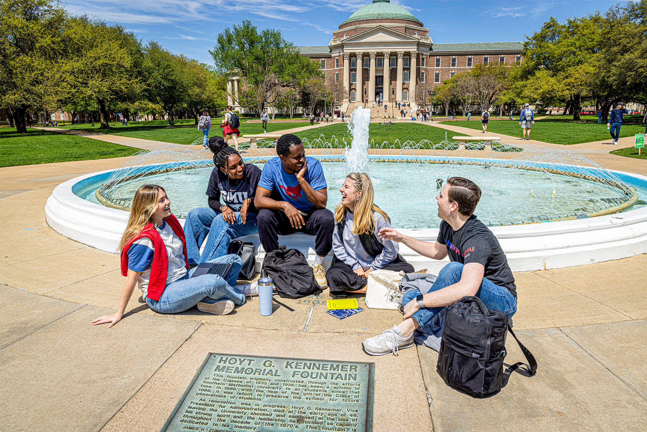 five students sitting outside by fountain in front of Dallas Hall on sunny day 