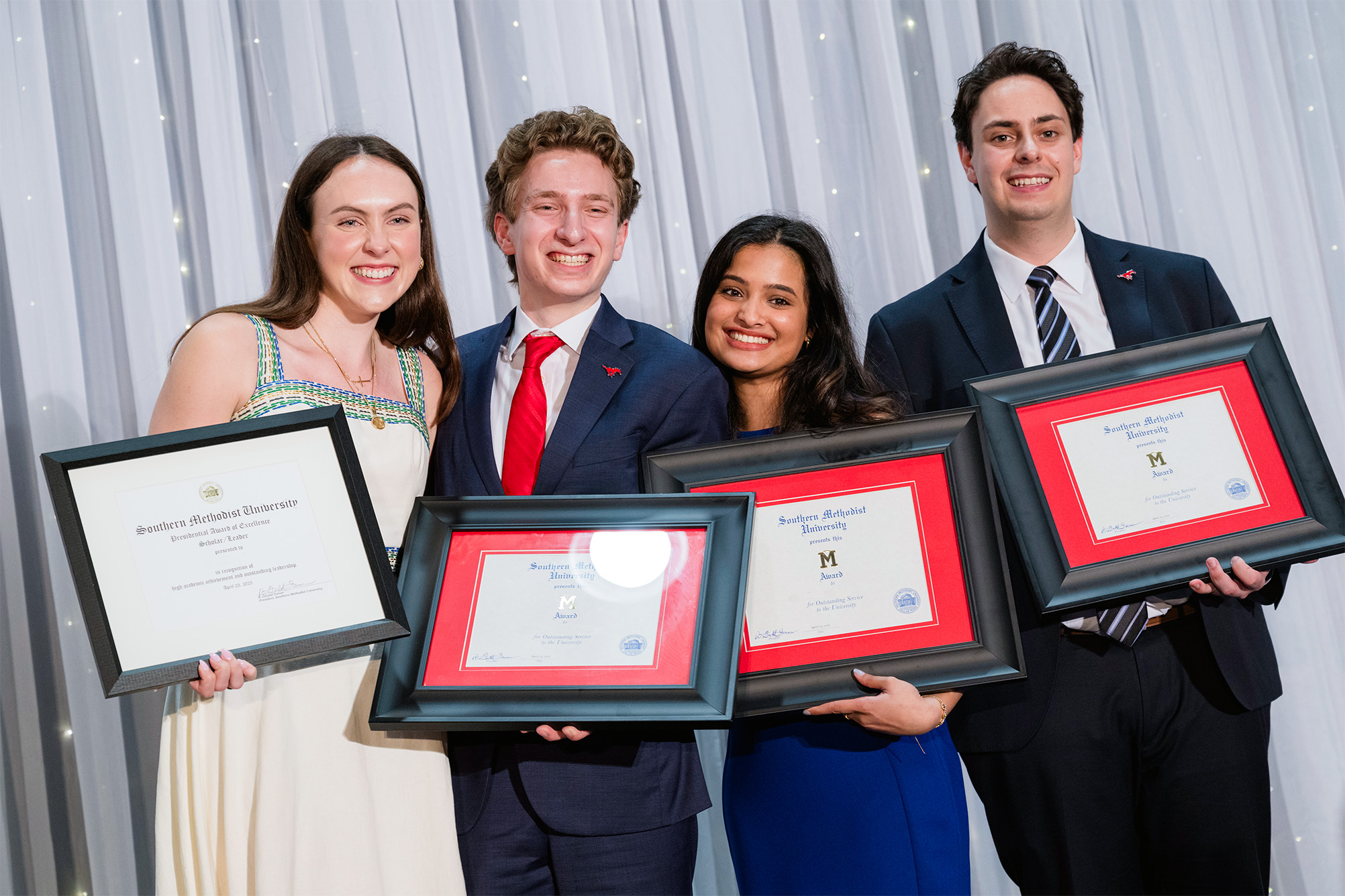 four students posing for photo with award certificates in front of white curtain backdrop