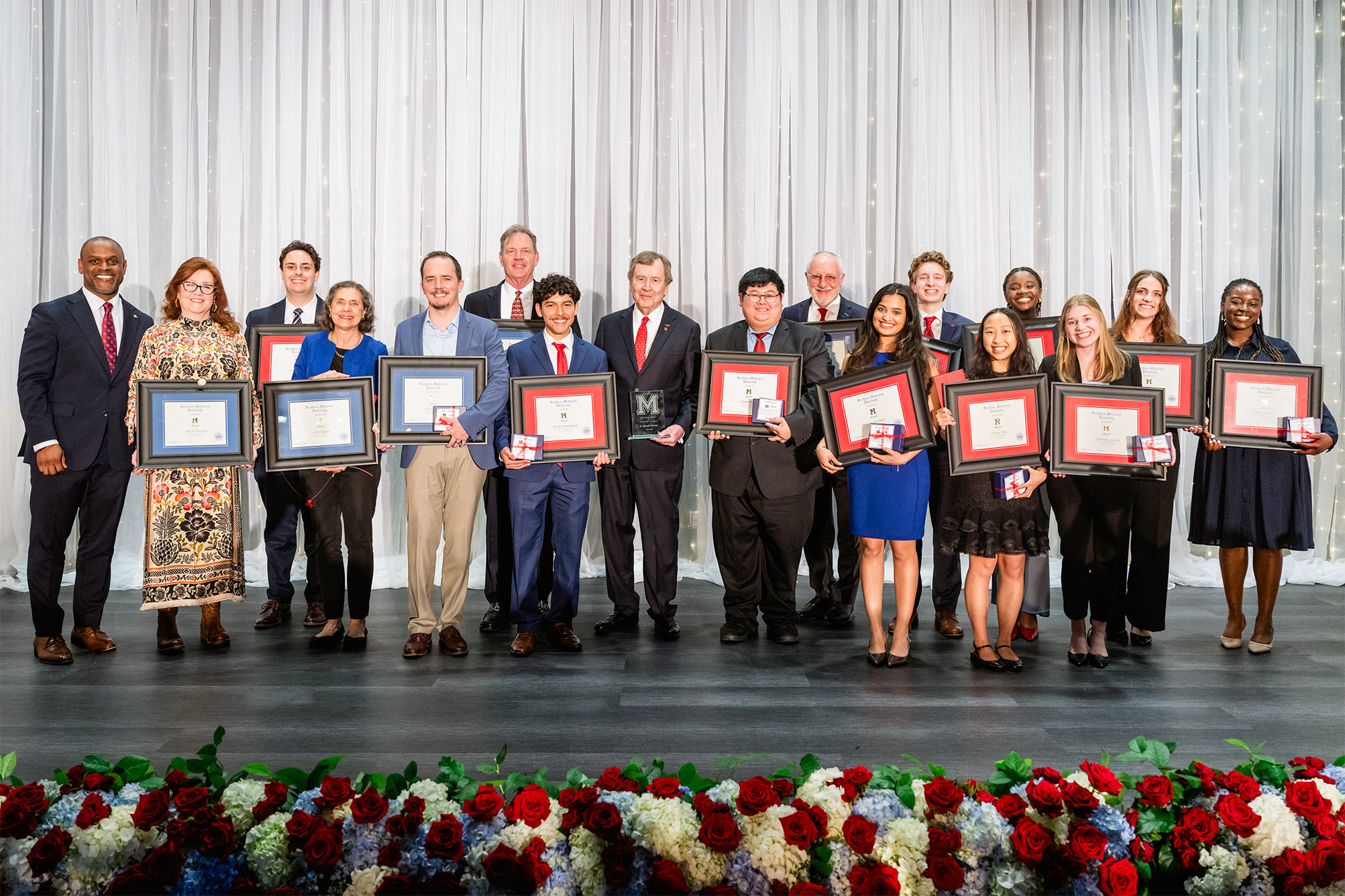 a group of award recipients posing for photo on stage with white curtain backdrop
