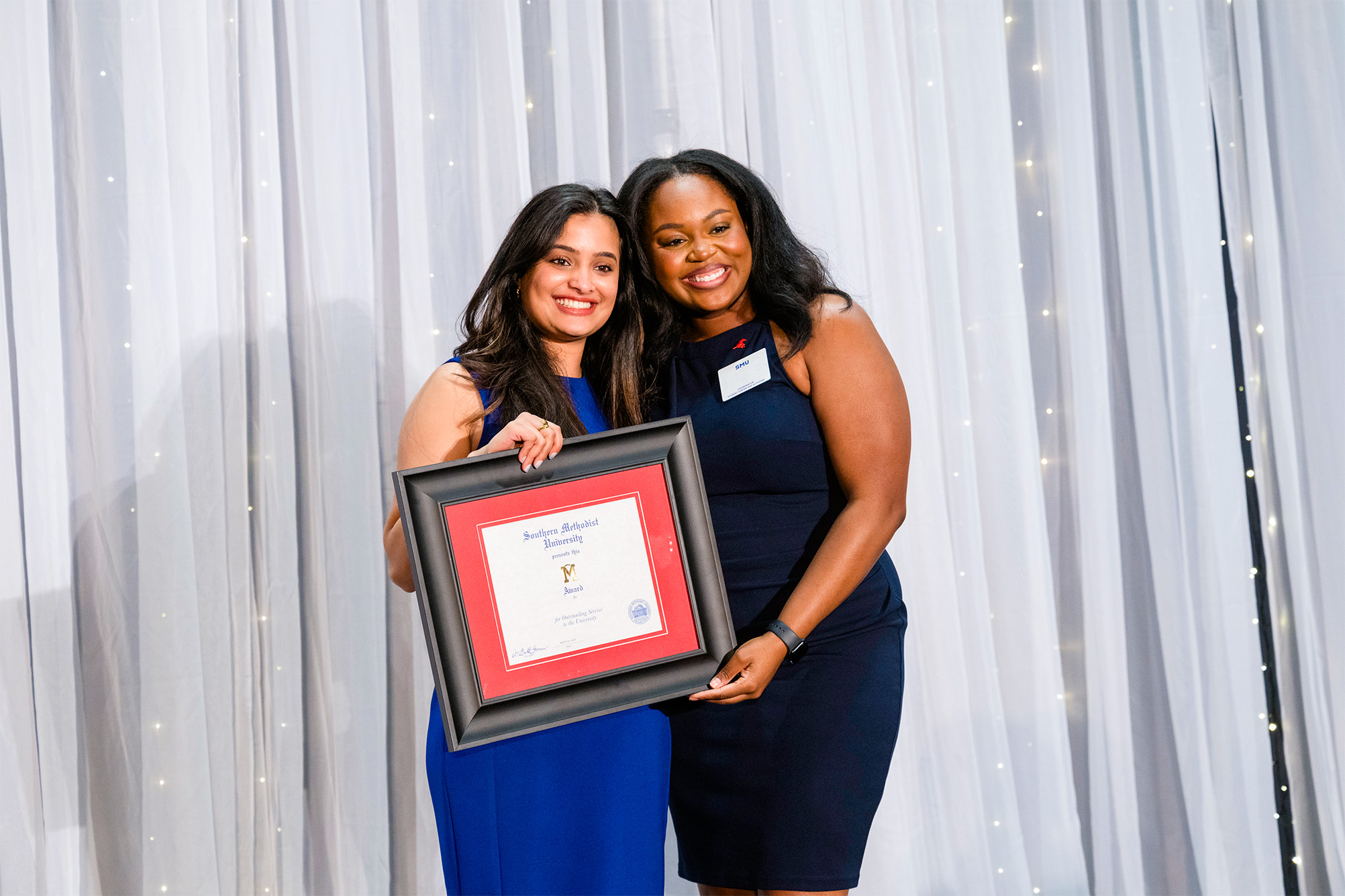 student standing with staff member posing for photo with award certificate in front of white curtain backdrop