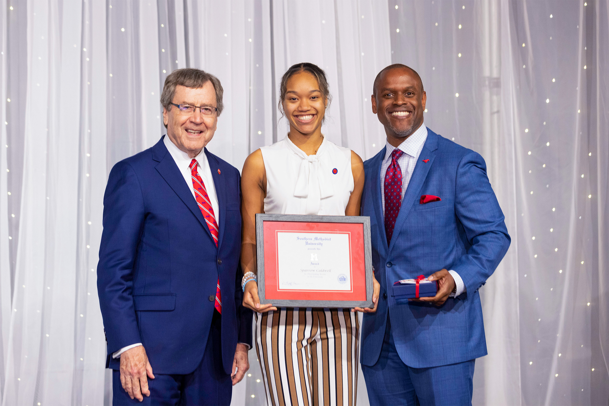 Dr. Gerald R. Turner, University President, Sparrow Caldwell, M Award Recipient, Dr. K.C. Mmeje, Vice President for Student Affairs in front of white sheer curtains with string lights